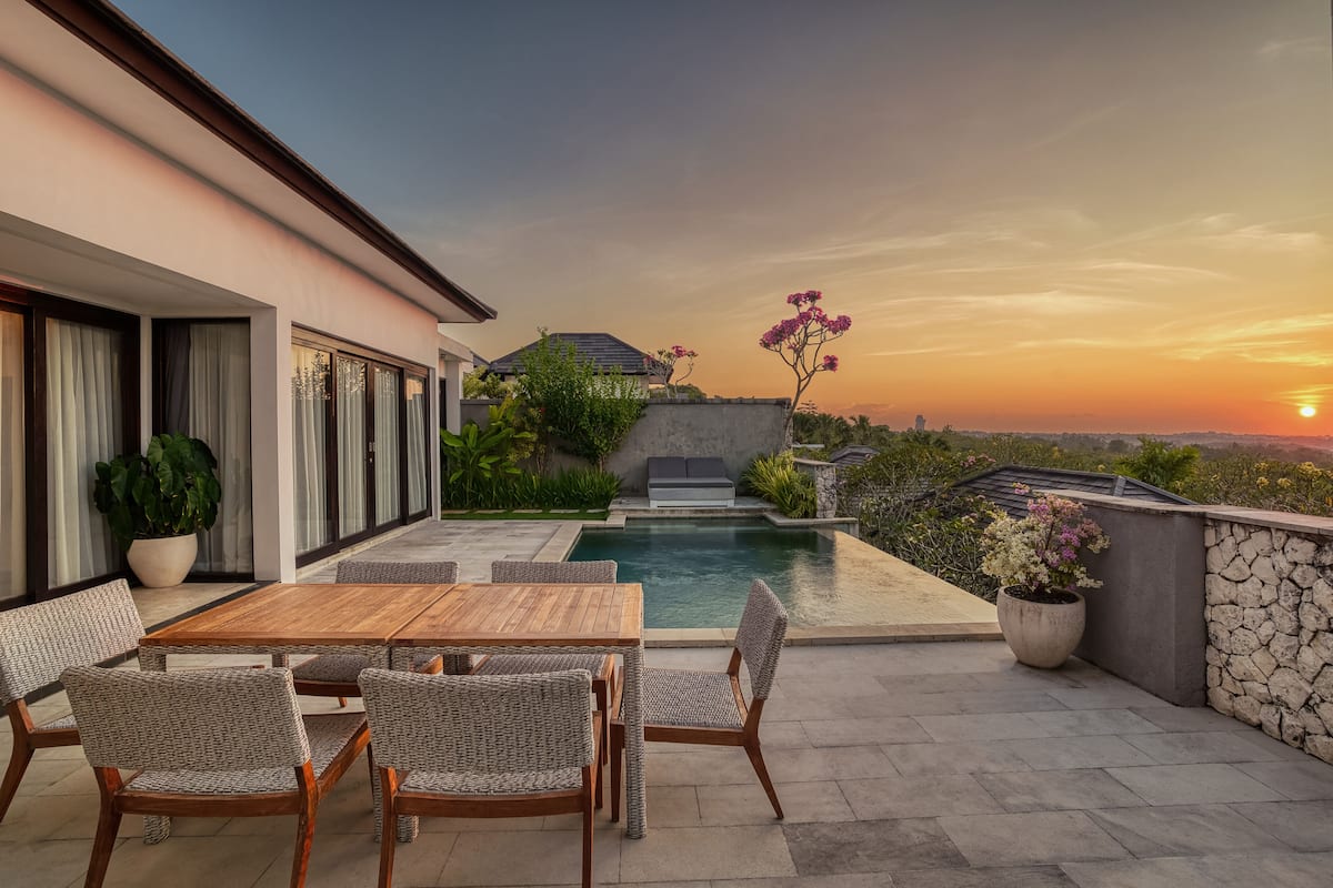 Un patio moderno al aire libre con piscina, zona de comedor y vistas al atardecer.