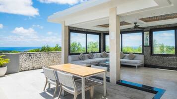 Une terrasse extérieure moderne, dotée d’une table et de chaises, d’un canapé et de grandes fenêtres offrant une vue sur l’océan.