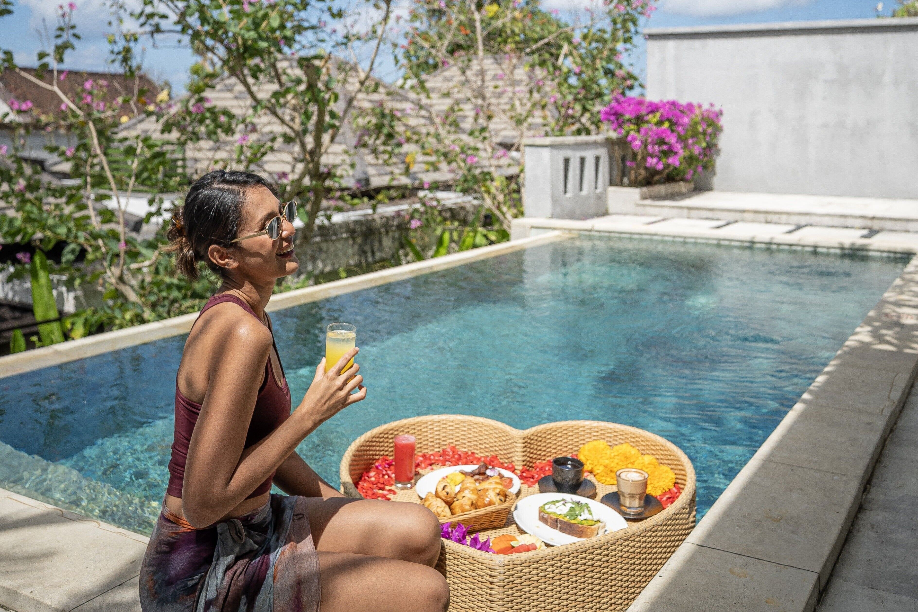 A person sitting by a pool with a drink and a basket of food.
