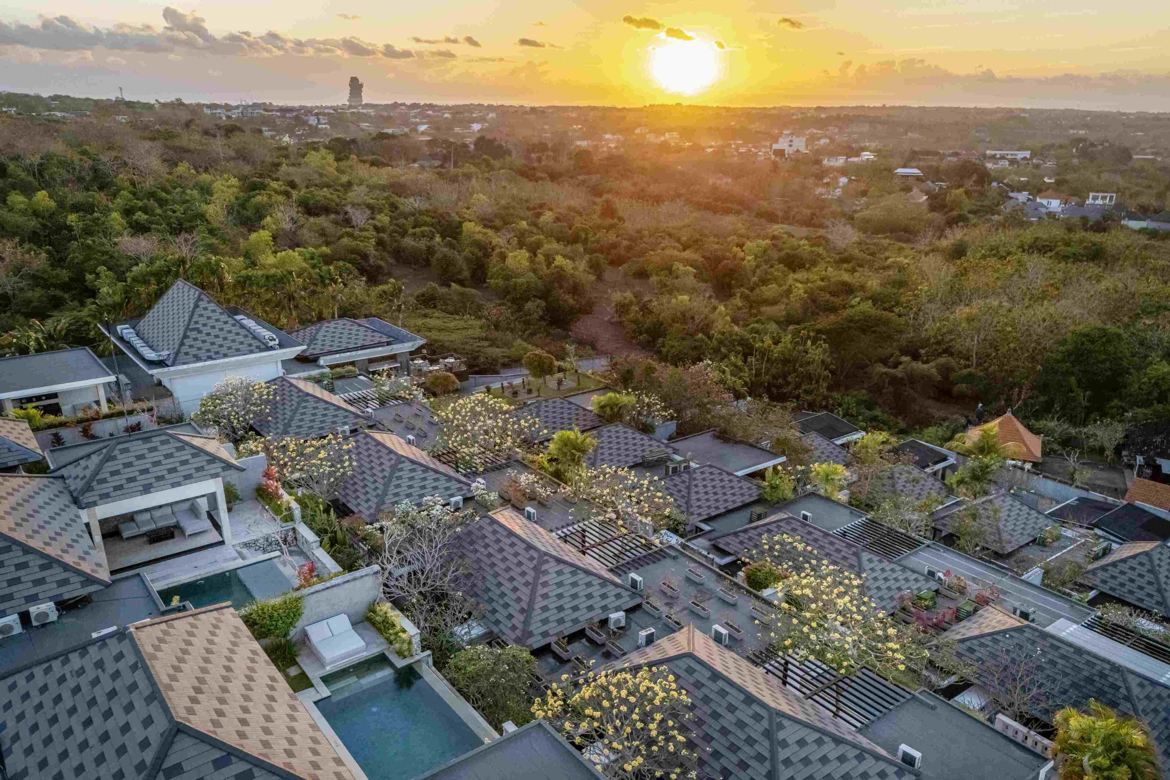 A residential area with multiple houses, a swimming pool, and a sunset in the background.