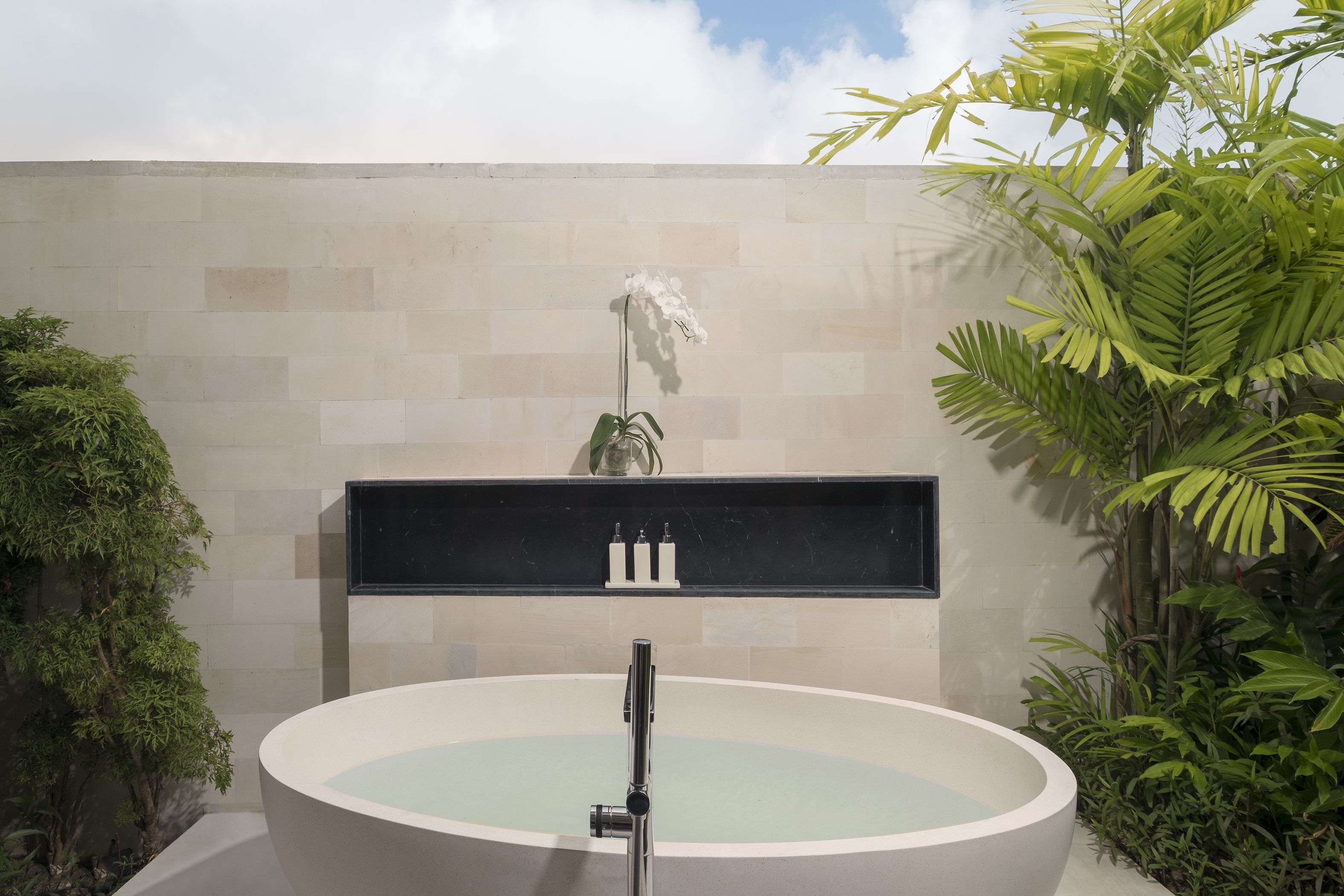 A modern bathroom with a freestanding bathtub, a marble countertop, and a potted orchid.
