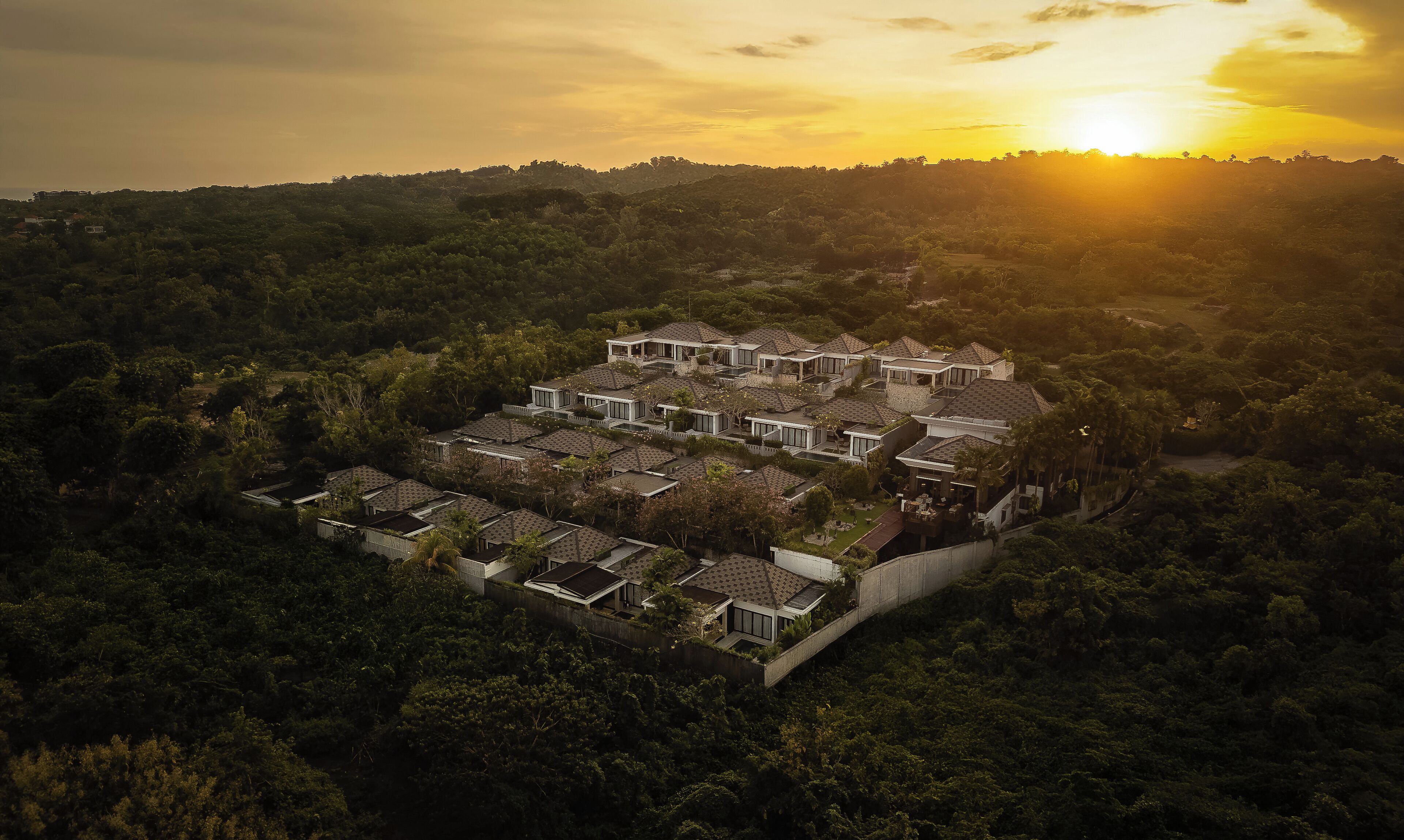 Zona residencial con varias casas rodeadas de abundante vegetación, destacando una casa con un amplio camino de entrada y un puente visible que conecta diferentes áreas.