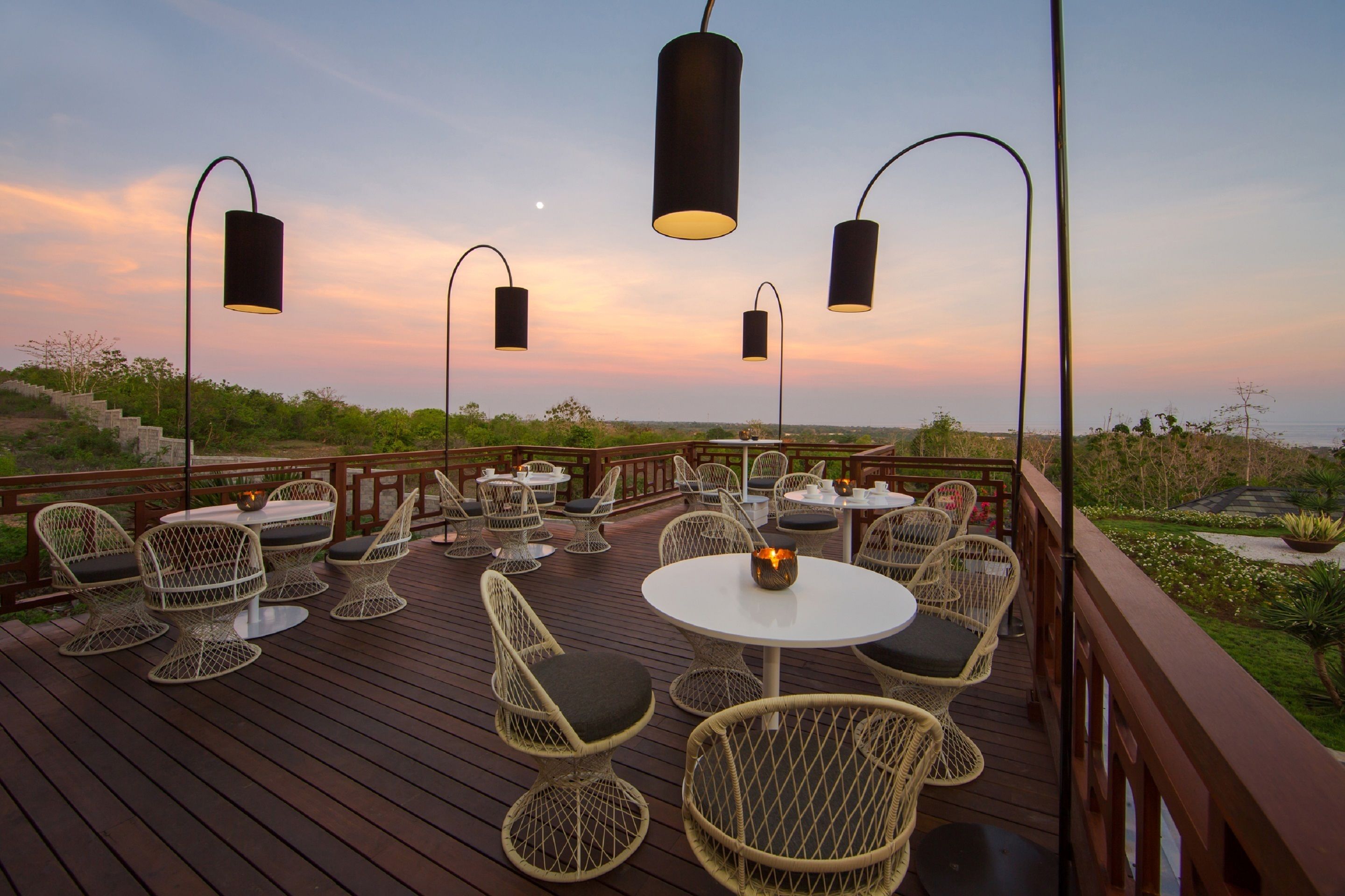 A deck with wicker chairs and tables, outdoor lighting, and a view of the landscape.