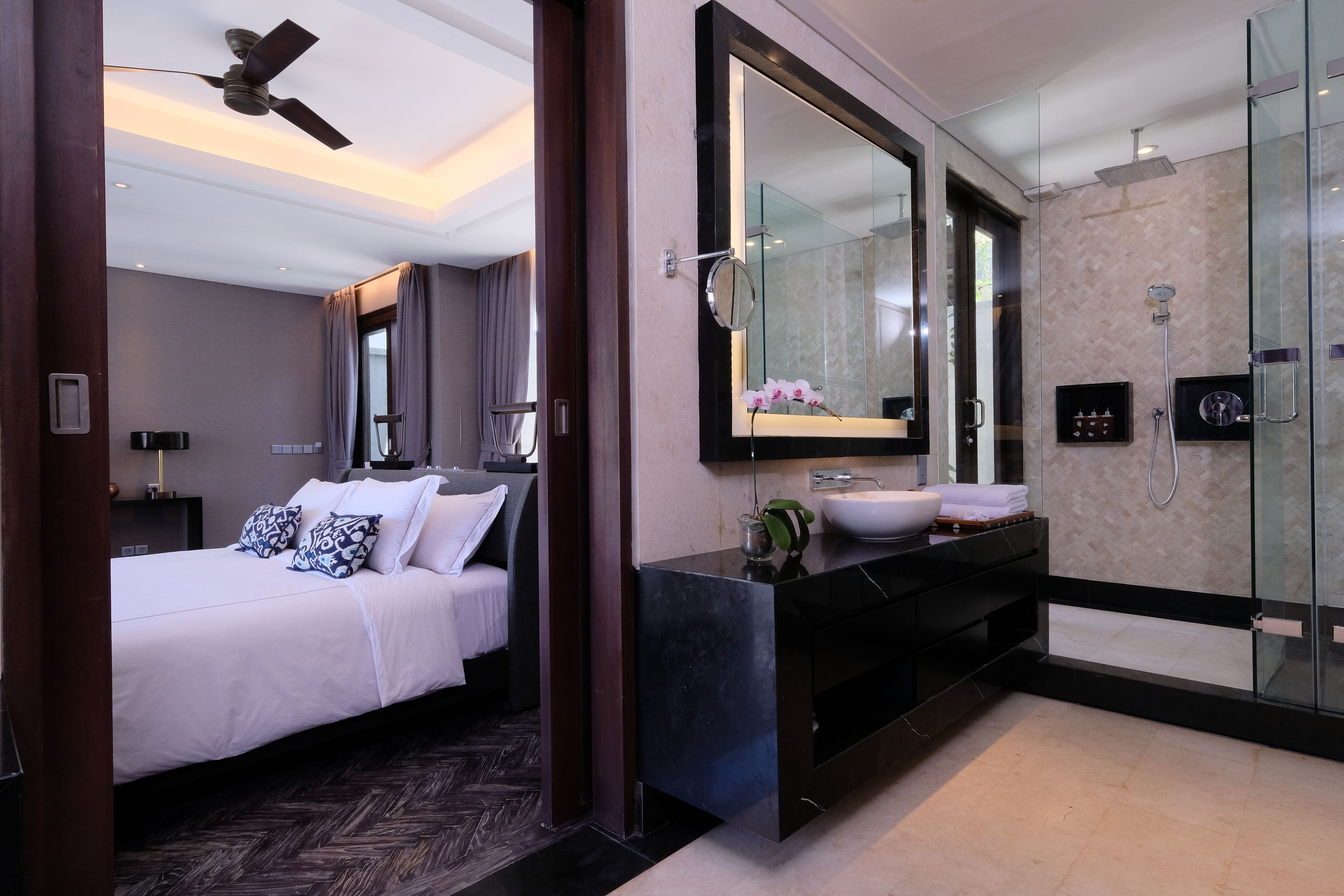 A modern hotel room with a large bed, a bathroom with a glass shower enclosure, and a large mirror.