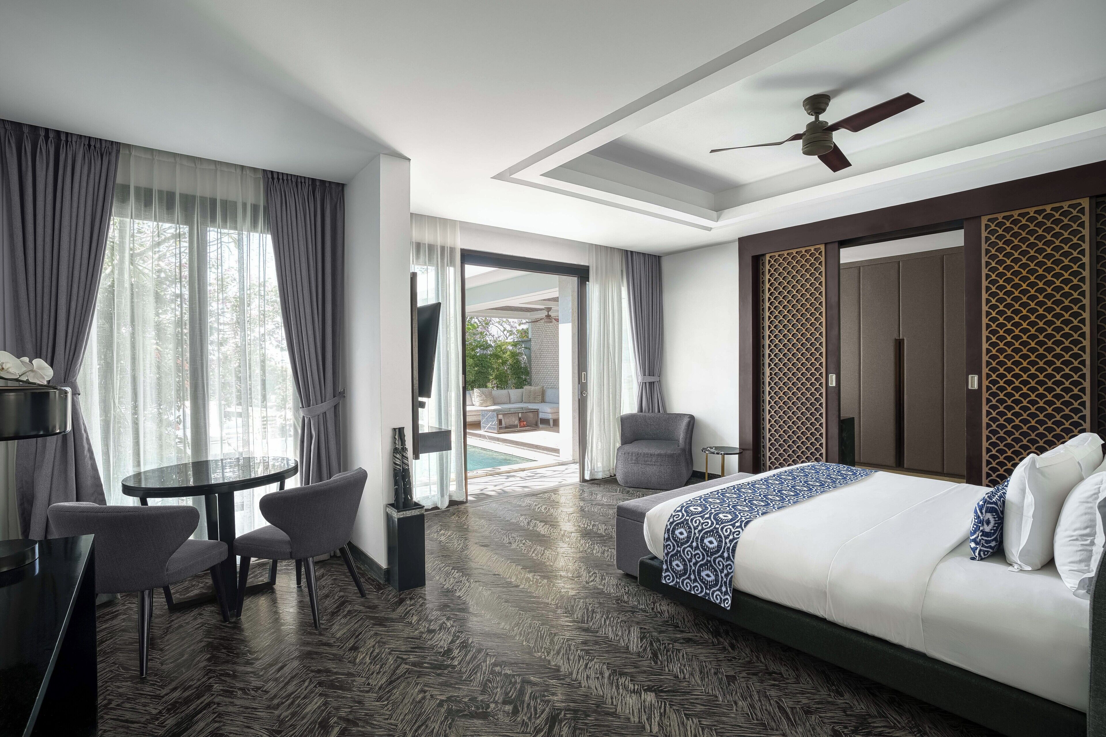 Een moderne hotelkamer met een groot bed, een ronde tafel met stoelen, een plafondventilator en uitzicht op het buiten.
