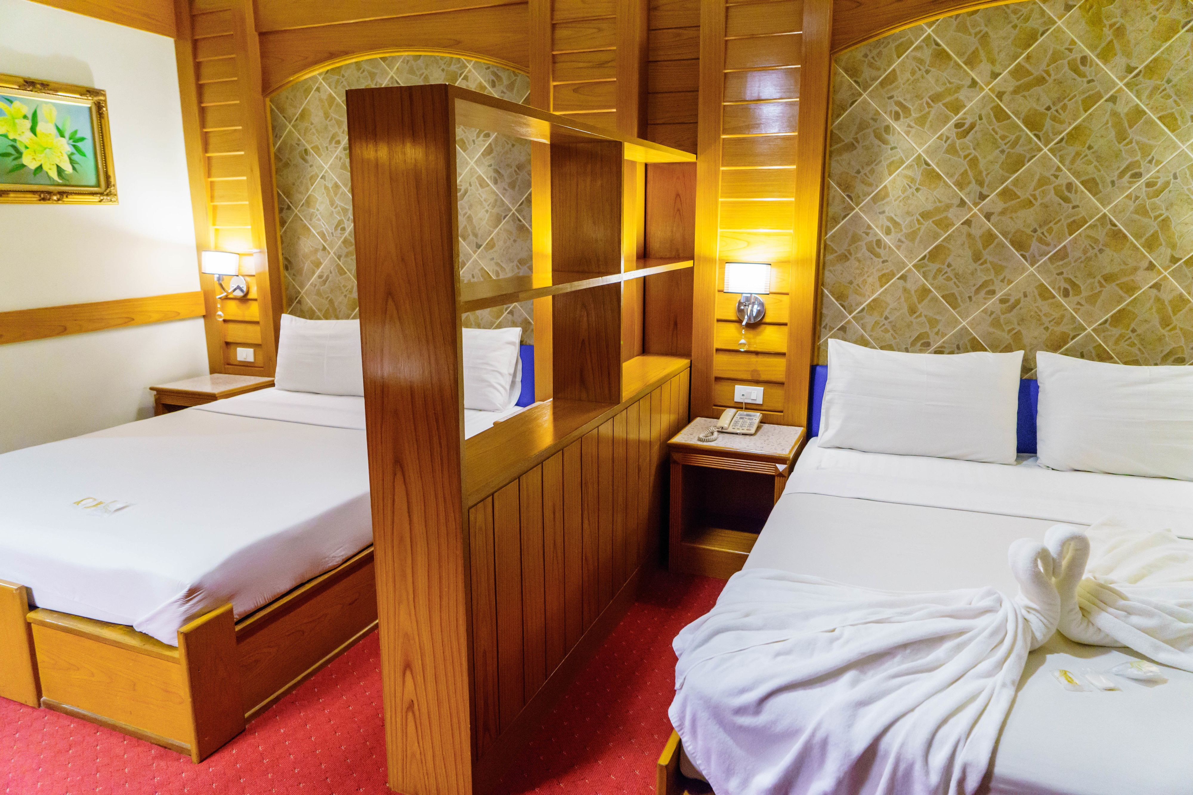 A hotel room with two beds, wooden paneling, a small table, and a nightstand with a lamp.
