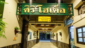 A hallway with a green sign, potted plants, and a stone wall. - Siri Hotel (Nakhon Ratchasima)