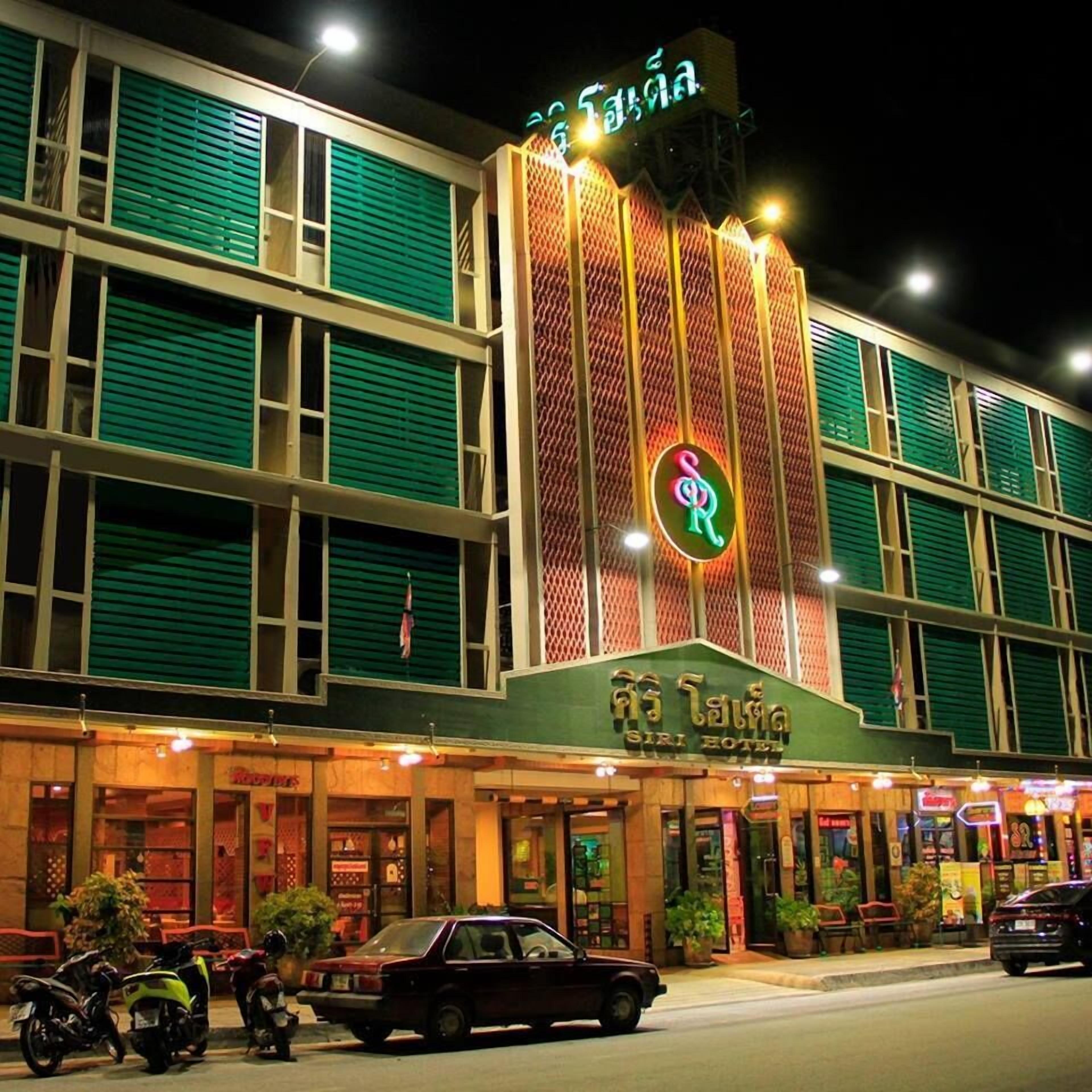 Un hotel con un letrero de neón, varios pisos y fachada verde.