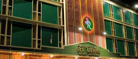 Un hotel con un letrero de neón, varios pisos y fachada verde.