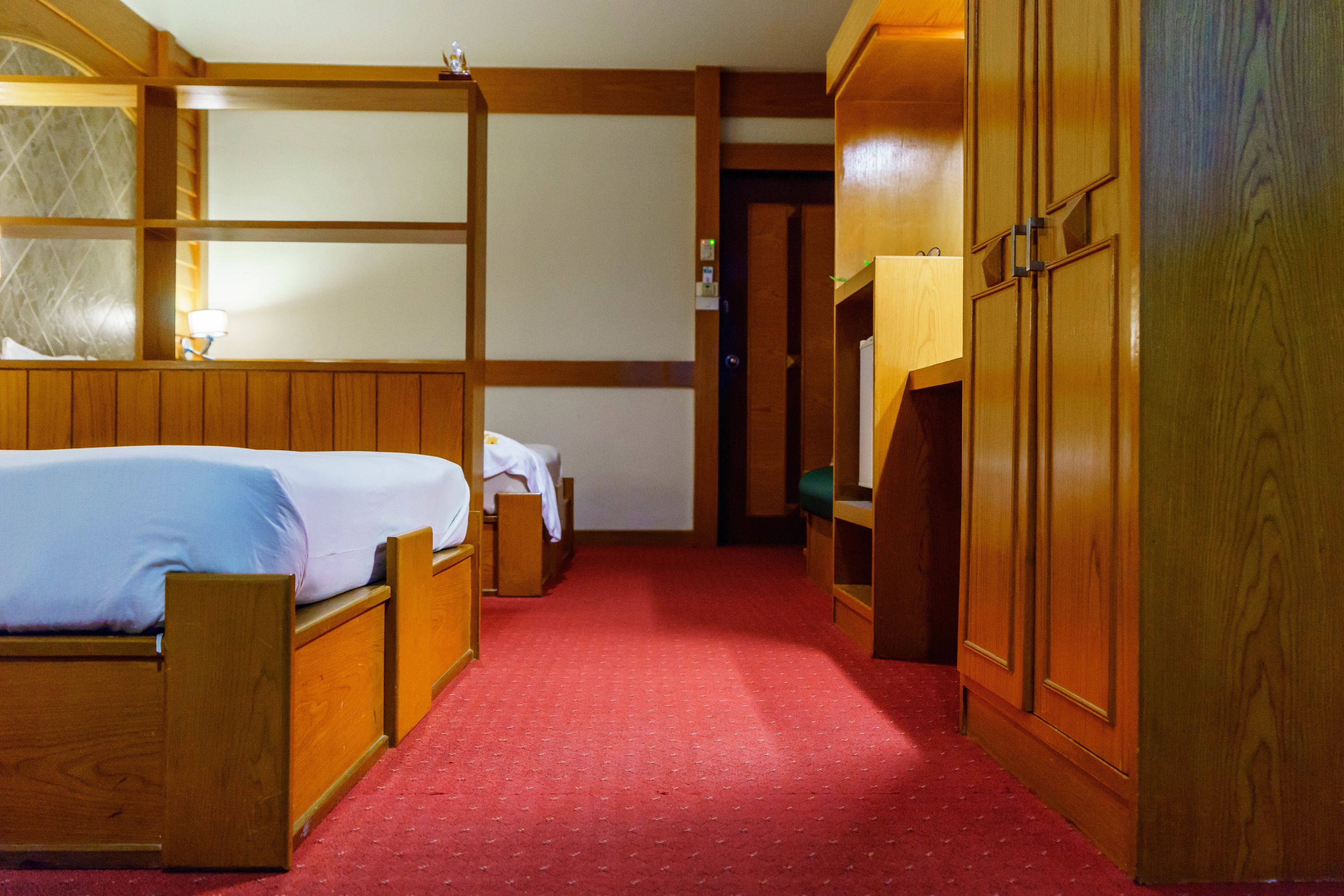 Una habitación de hotel con una cama de madera, alfombra roja y armarios de madera.