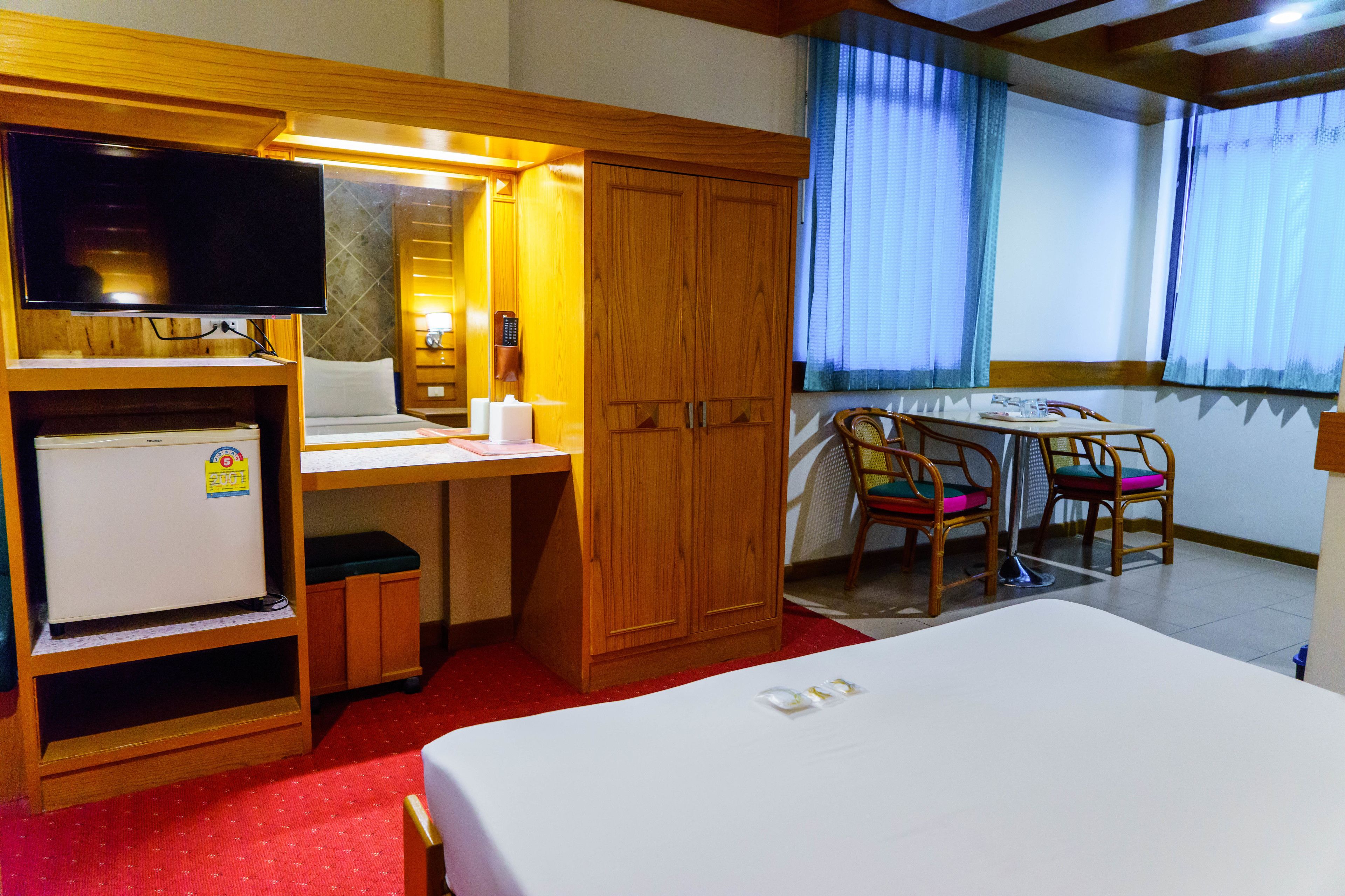 Una habitación de hotel compacta con cama, escritorio, silla, refrigerador pequeño, televisor y armario.