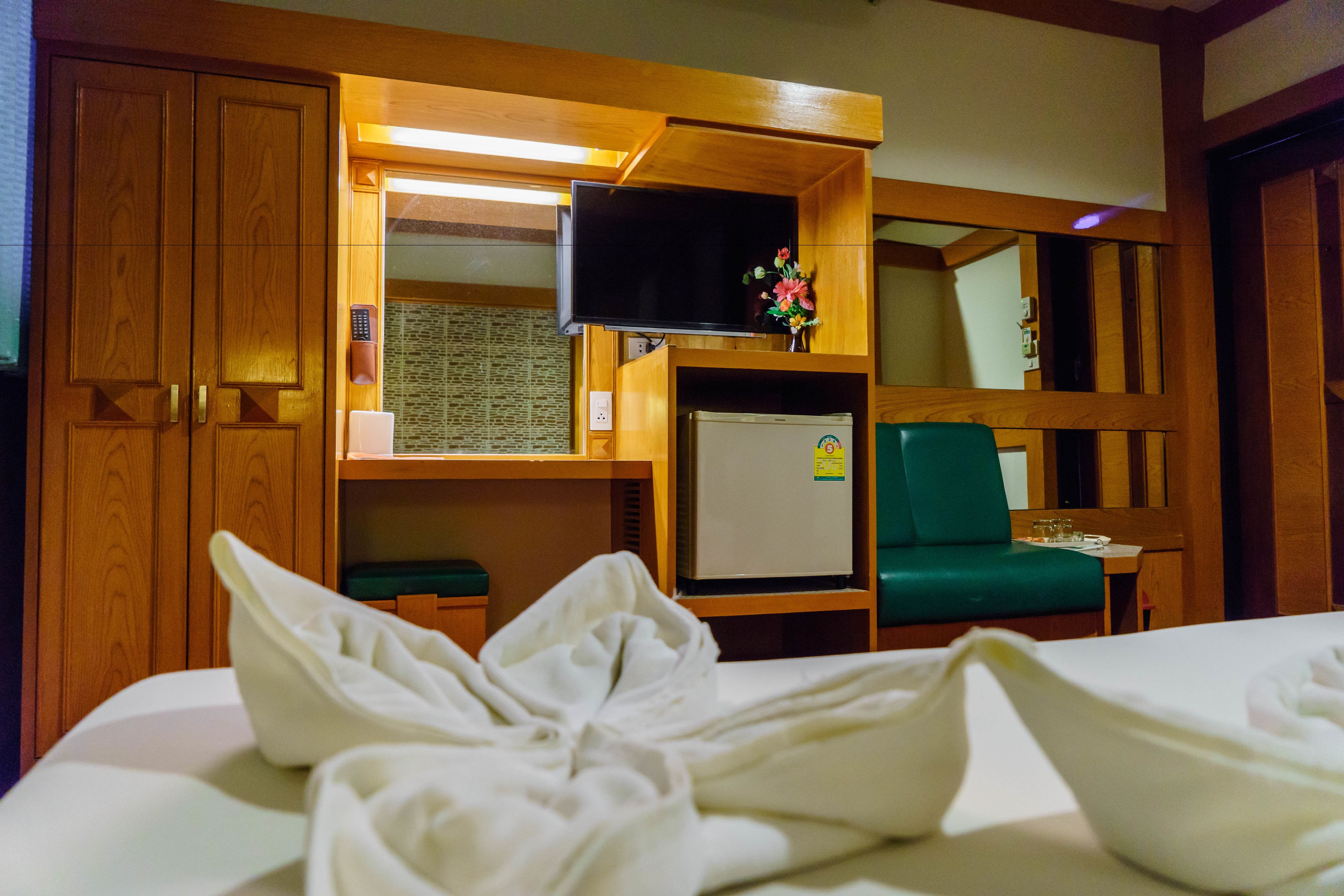 A hotel room with a bed, a television, a refrigerator, a green chair, and wooden walls.
