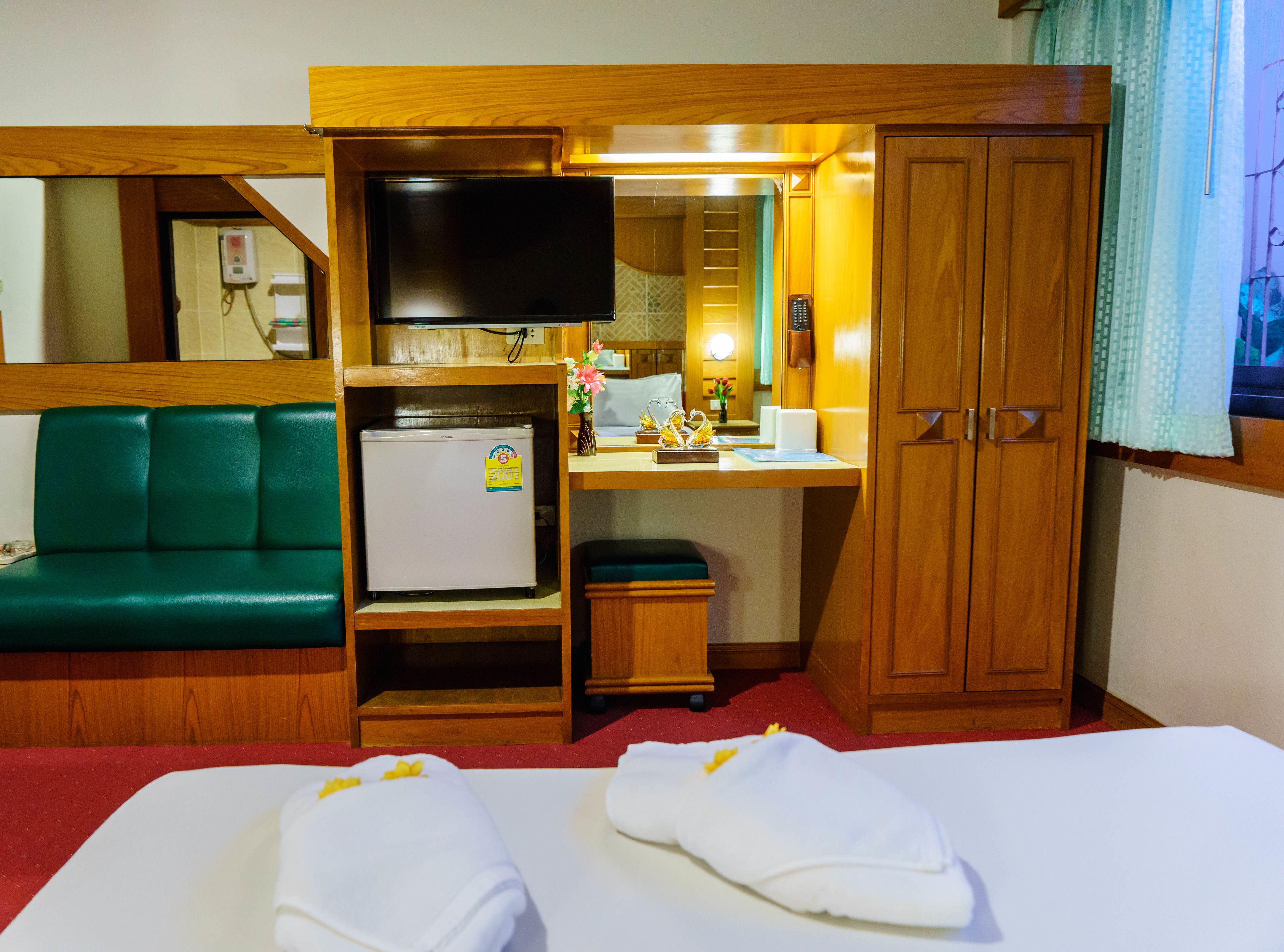 A hotel room with a bed, a desk with a television, a refrigerator, a green sofa, and a wooden wardrobe.