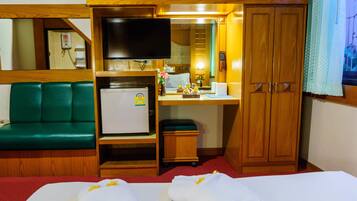Habitación de hotel con cama, escritorio con televisor, refrigerador, sofá verde y armario de madera.