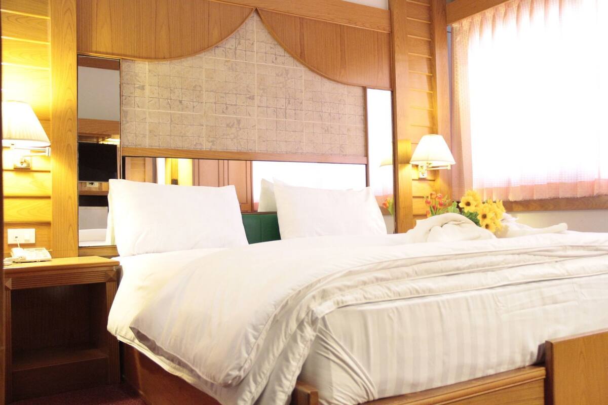 A hotel room with a large bed, wooden headboard, two bedside tables, and a window with curtains.