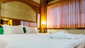 A hotel room with a large bed, a headboard with a wooden panel, and a window with curtains. - Siri Hotel (Nakhon Ratchasima)