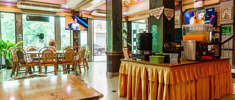 A restaurant with a bar area, wooden chairs, a counter with a yellow tablecloth, and a television screen.