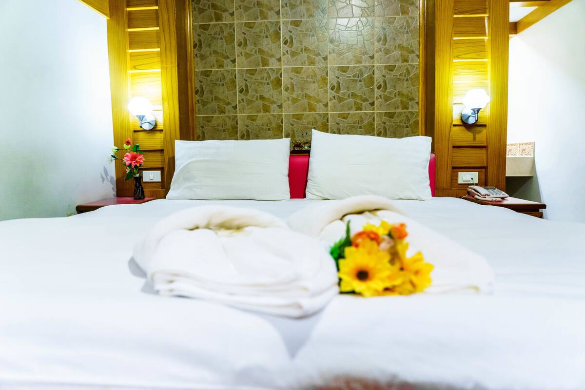 A hotel room with a neatly made bed, a vase with flowers, and a wall with a textured pattern.