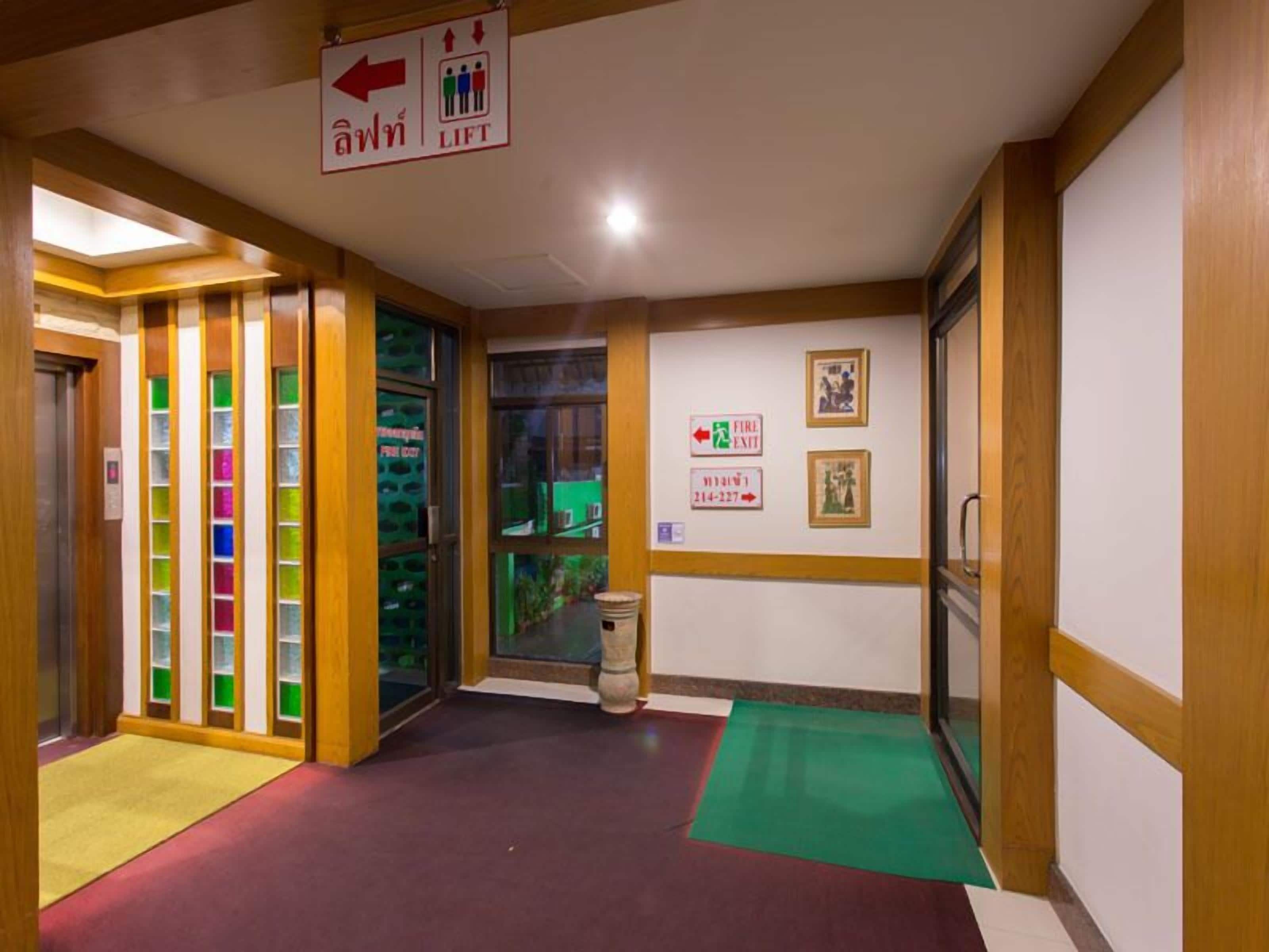 A hallway with a sign indicating a lift direction, a fire exit sign, and a fire alarm pull station.
