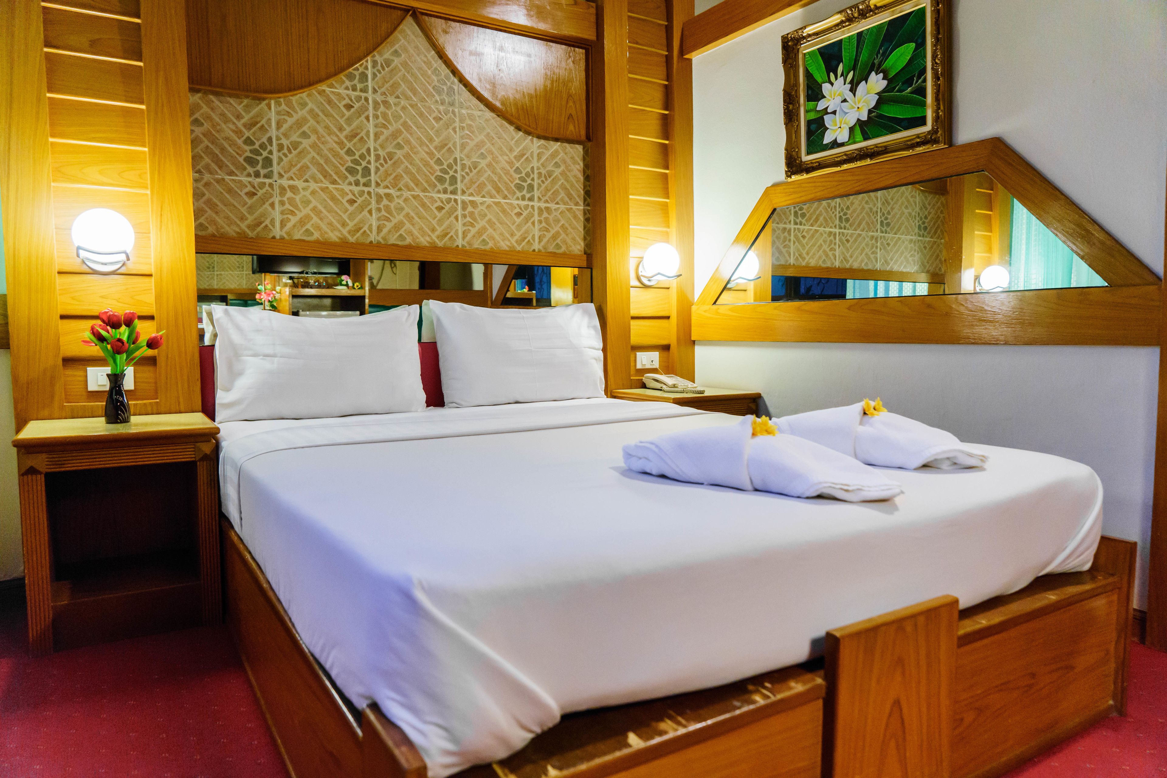 A hotel room with a large bed, wooden headboard, bedside tables, and a mirror.