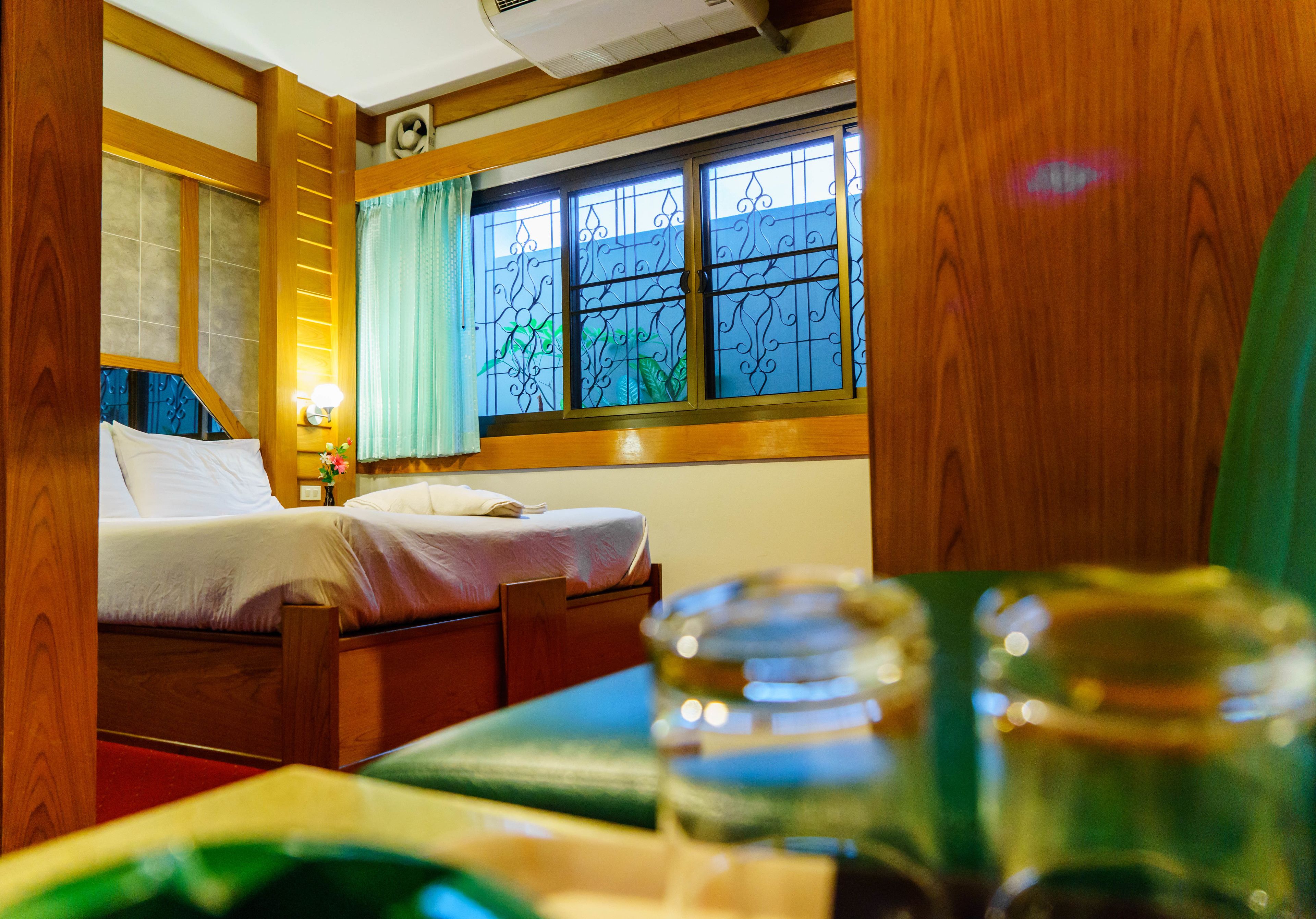 Ein raumförmiger Innenbereich mit Holzrahmen, zwei Betten, einem Fenster mit Gitterstäben und einem Nachttisch mit Lampe.