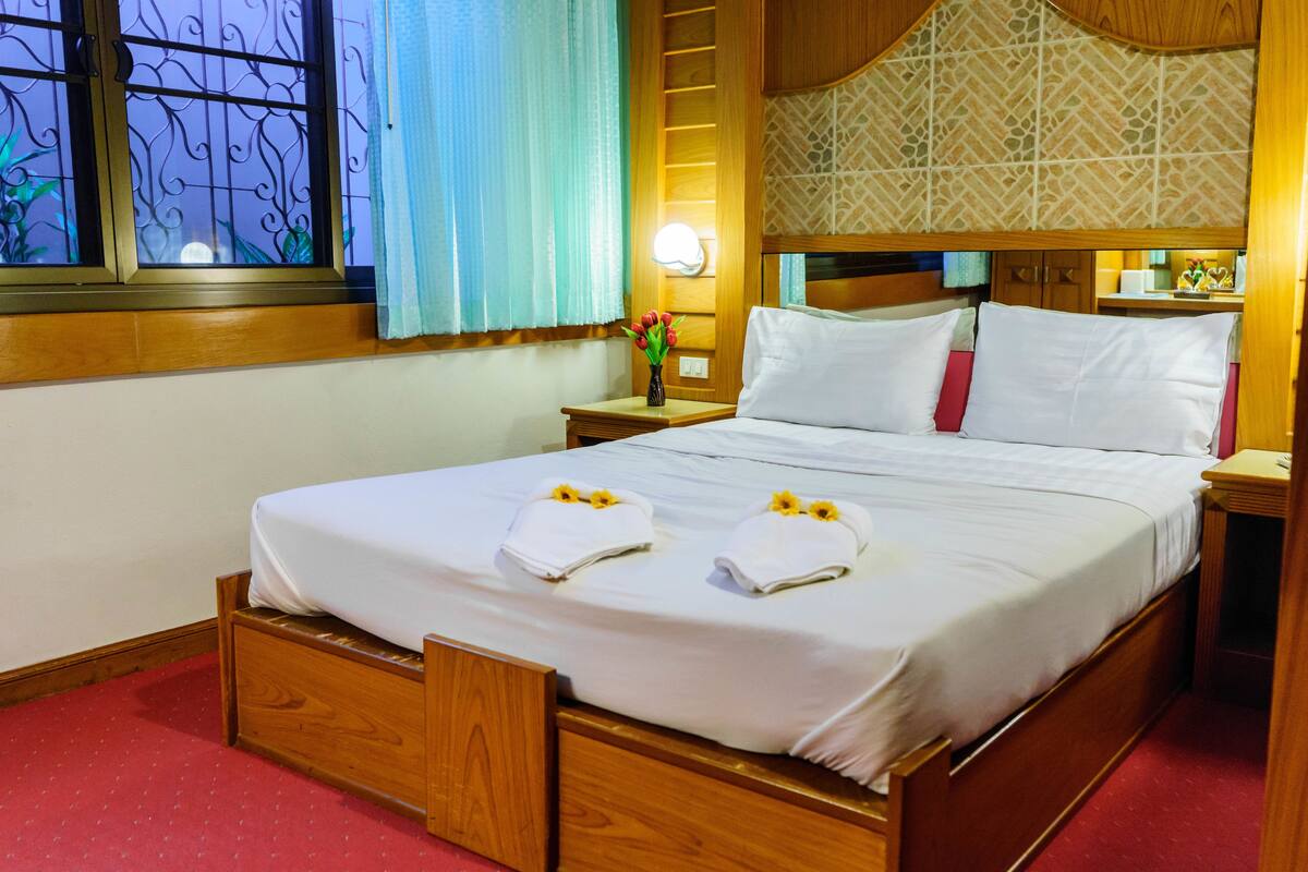 A neatly made bed with two towels and a vase of flowers on the nightstand.
