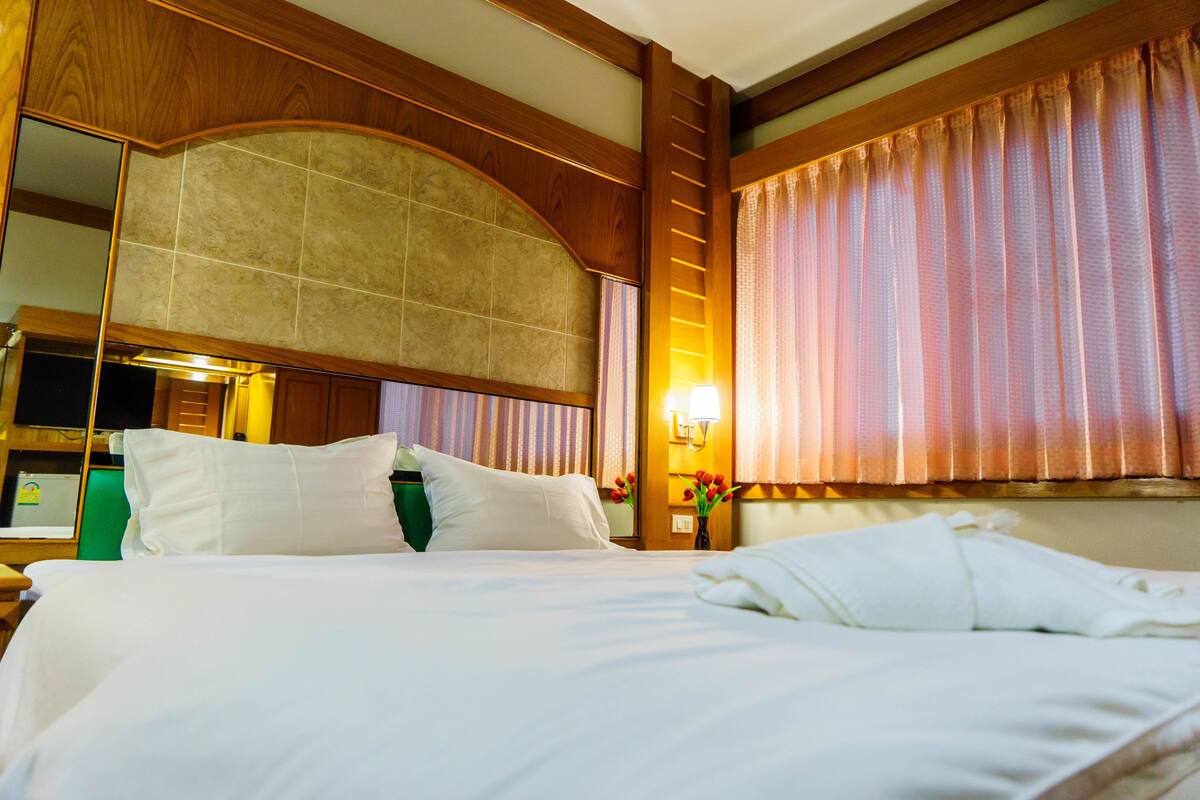 A hotel room with a large bed, a wooden headboard, a mirror, and a window with curtains.