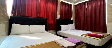 Habitación de hotel con dos camas, cortinas rojas, ropa de cama blanca y una manta marrón.
