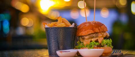 A burger with fries and a drink on a table with a blurred background of lights.