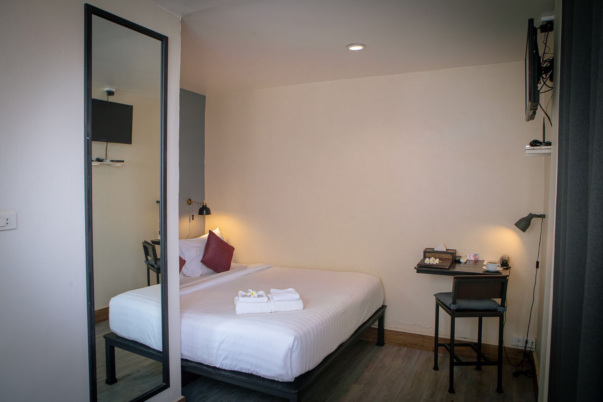 A hotel room with a bed, a desk, a chair, a TV mounted on the wall, and a mirror.