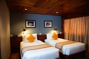 Habitación de hotel con dos camas, cabeceros de madera y cuadros enmarcados en la pared.