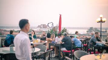 Un espace de restauration aménagé sur le toit, avec des tables et des chaises, offrant une vue sur le paysage urbain et un bâtiment situé au loin.