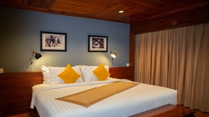 Un llit ben fet amb llençols blancs i dos coixins grocs, un tamboret de fusta al peu del llit, i dues làmpades penjades a la paret.