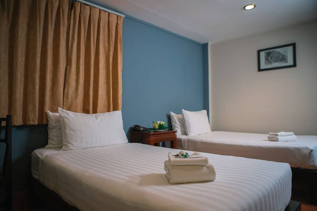 A hotel room with two beds, a nightstand with a phone and a flower, and a framed picture on the wall.