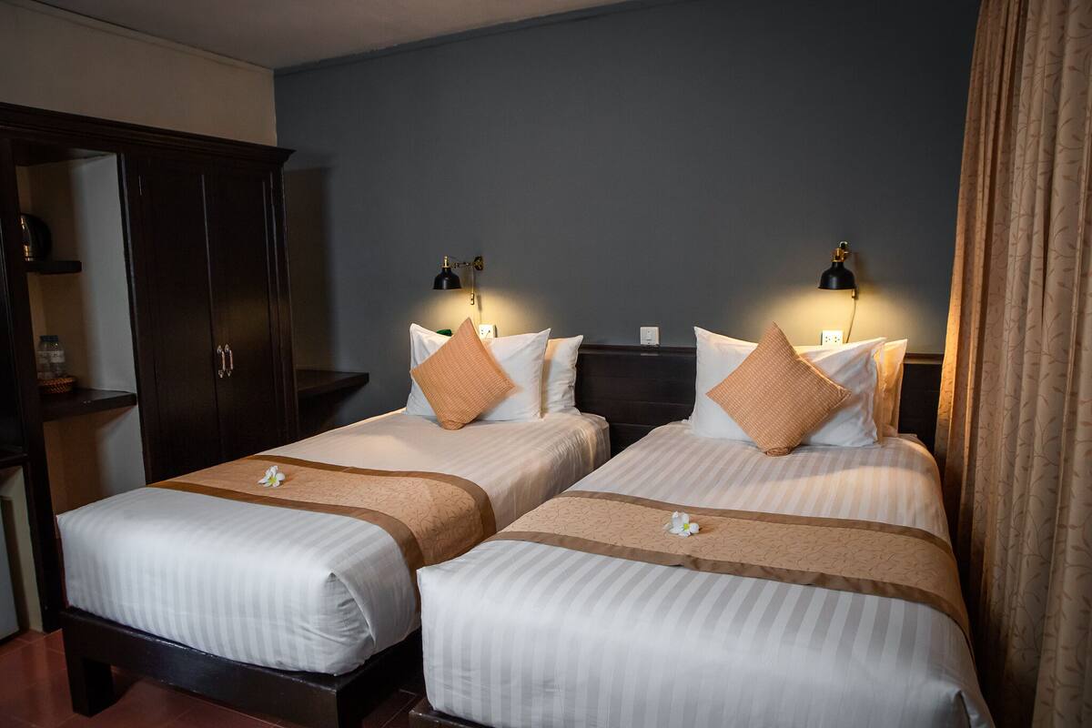 A hotel room with two beds, dark wooden wardrobe, and bedside lamps.