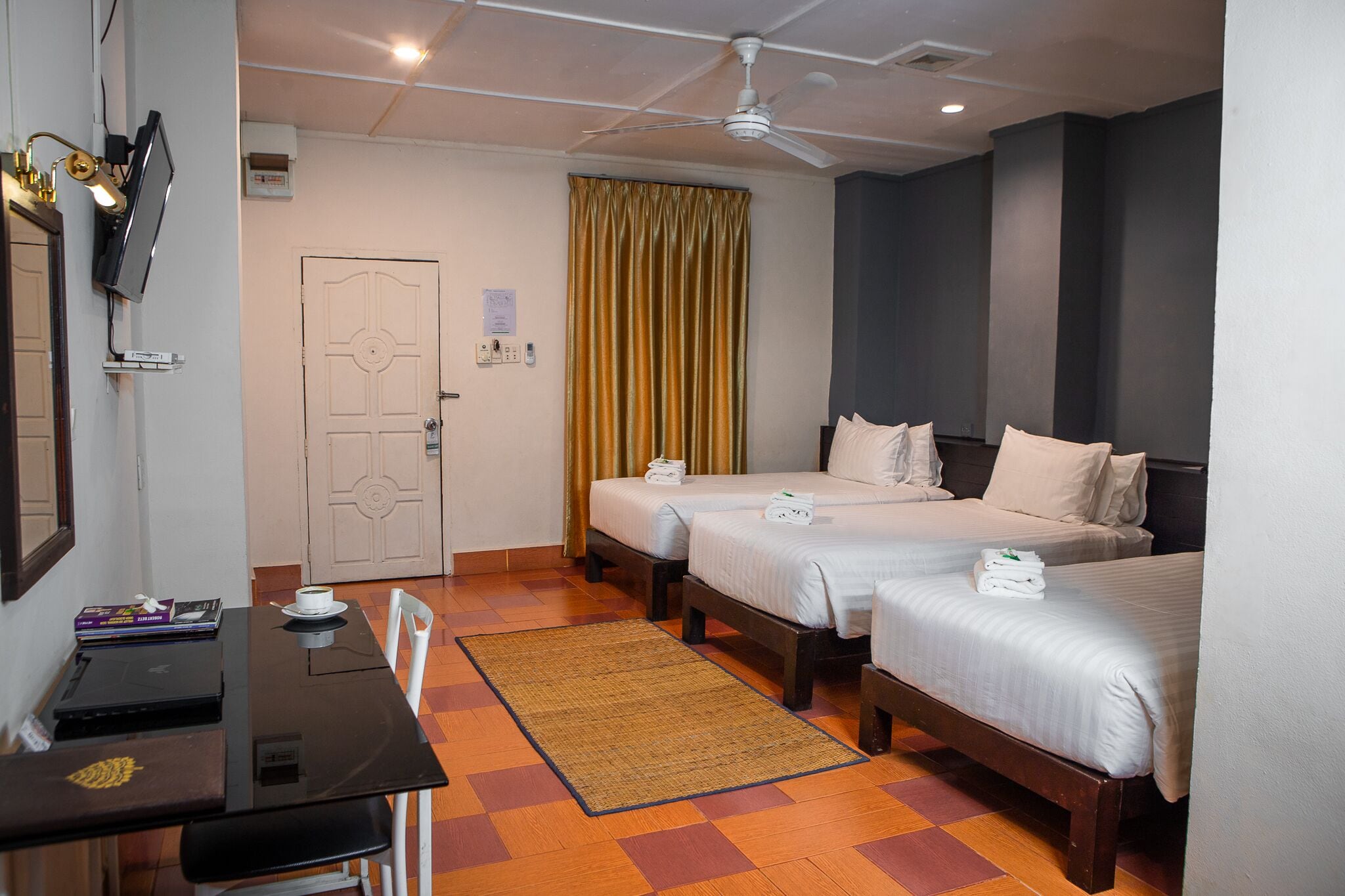 Una habitación de hotel con dos camas, un escritorio con una computadora portátil, un televisor y un ventilador de techo.