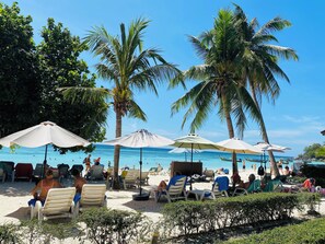 Uma praia com palmeiras, espreguiçadeiras e guarda-sóis.
