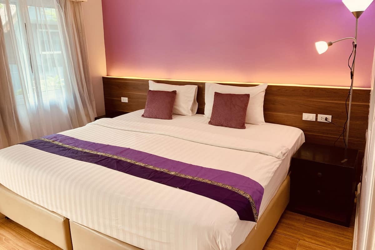 Une chambre d’hôtel avec un grand lit, une table de chevet, une lampe et une fenêtre avec des rideaux.