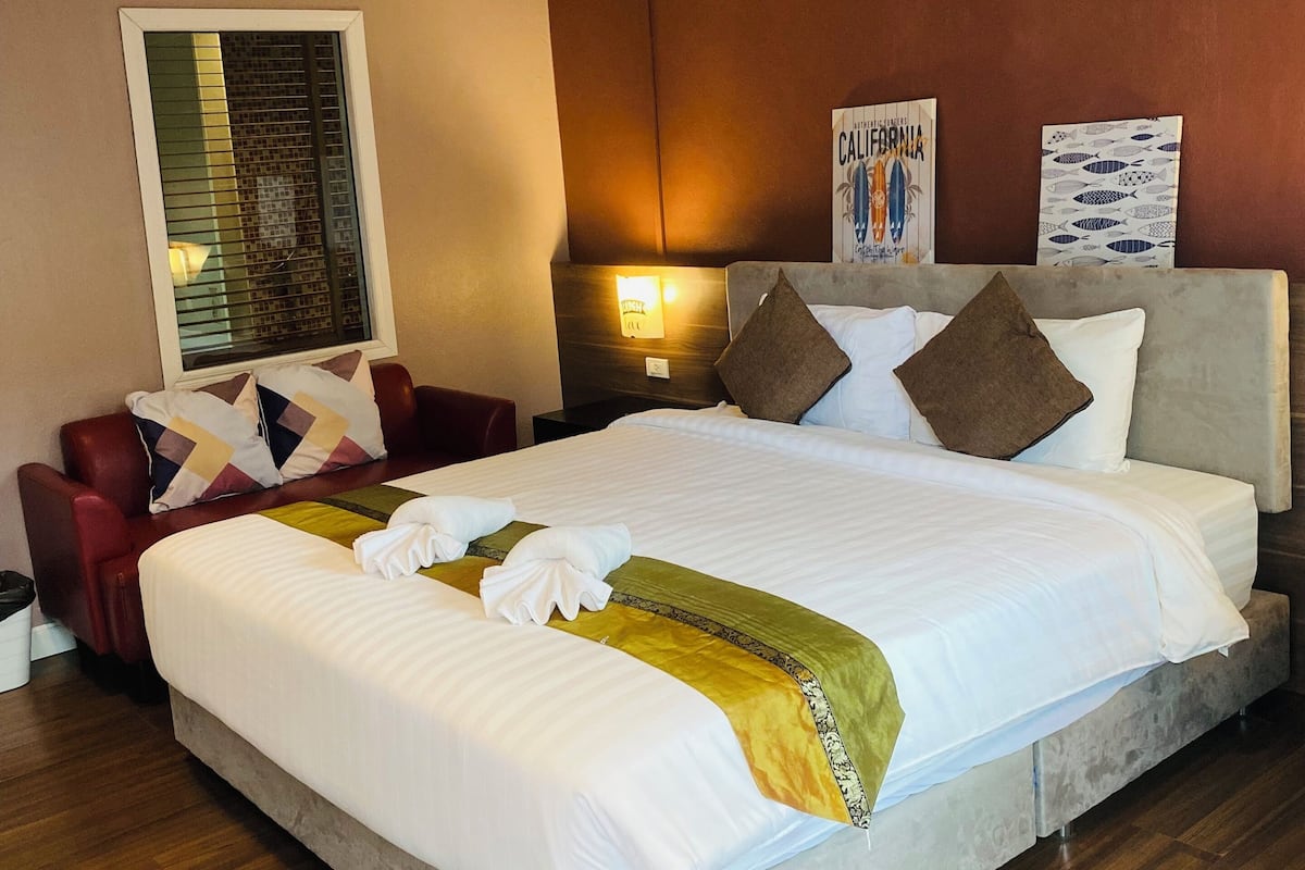 Hotelkamer met een groot bed, een rode fauteuil, een nachtkastje met lamp en twee kunstwerken aan de muur.