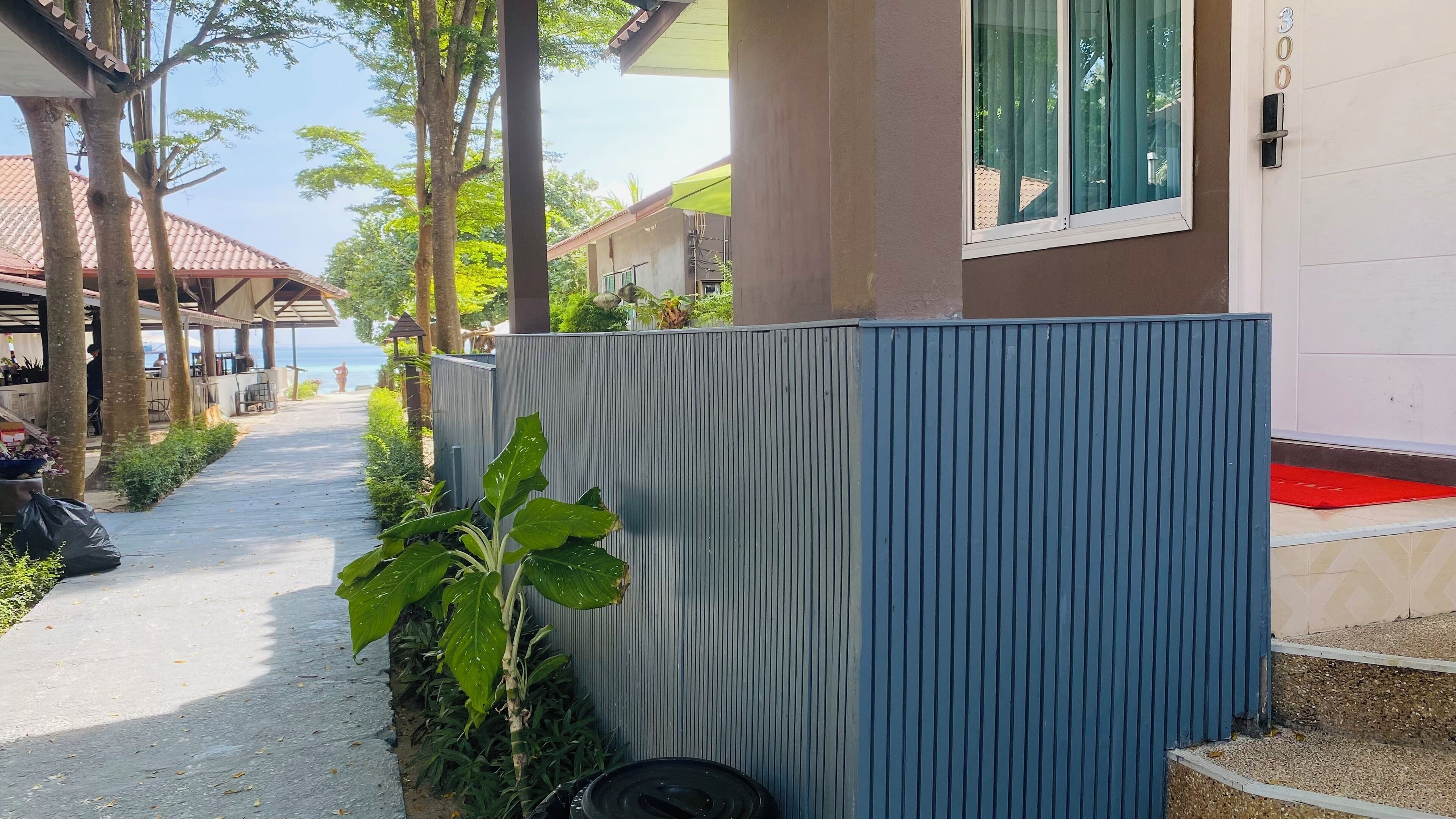 A pathway leading to a building with a blue exterior wall, a red carpet, and a view of the sea.