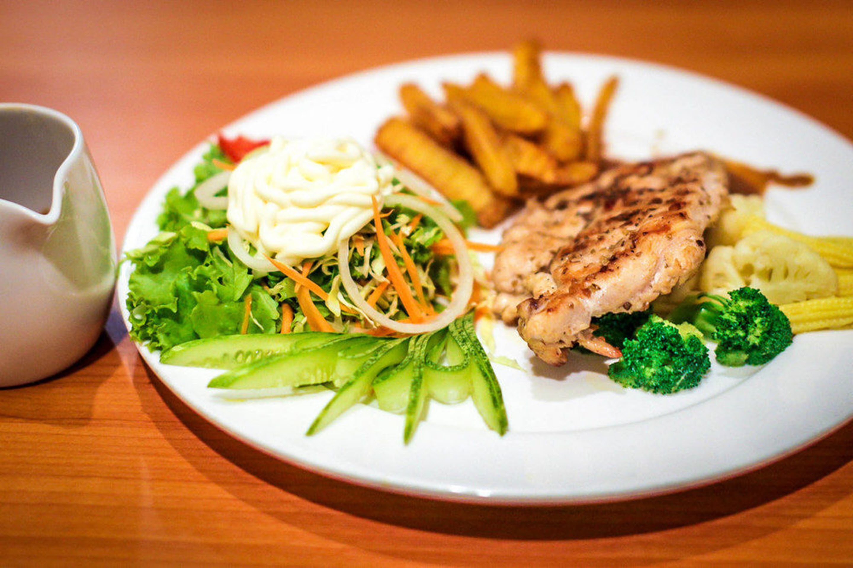 Un plato con pollo a la parrilla, papas fritas, ensalada y una guarnición de maíz.