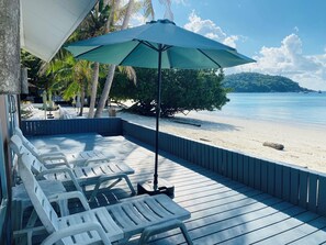 A wooden deck with white plastic lounge chairs and a green umbrella, overlooking a beach with palm trees and a clear sky. - Bella Vista Beach Resort Koh Lipe (Koh Lipe)