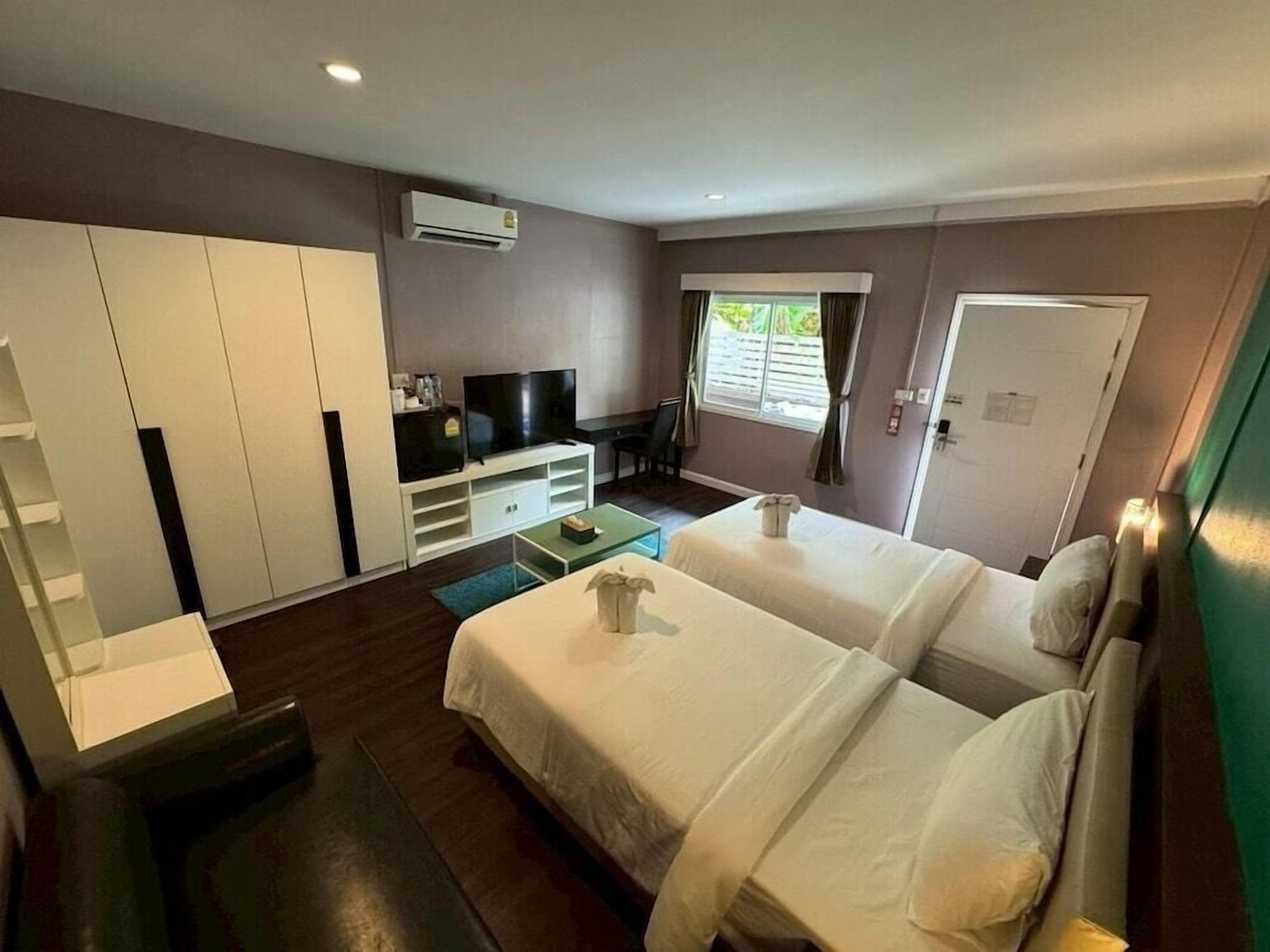 Una habitación de hotel con dos camas, televisión, armario y ventana con cortinas.