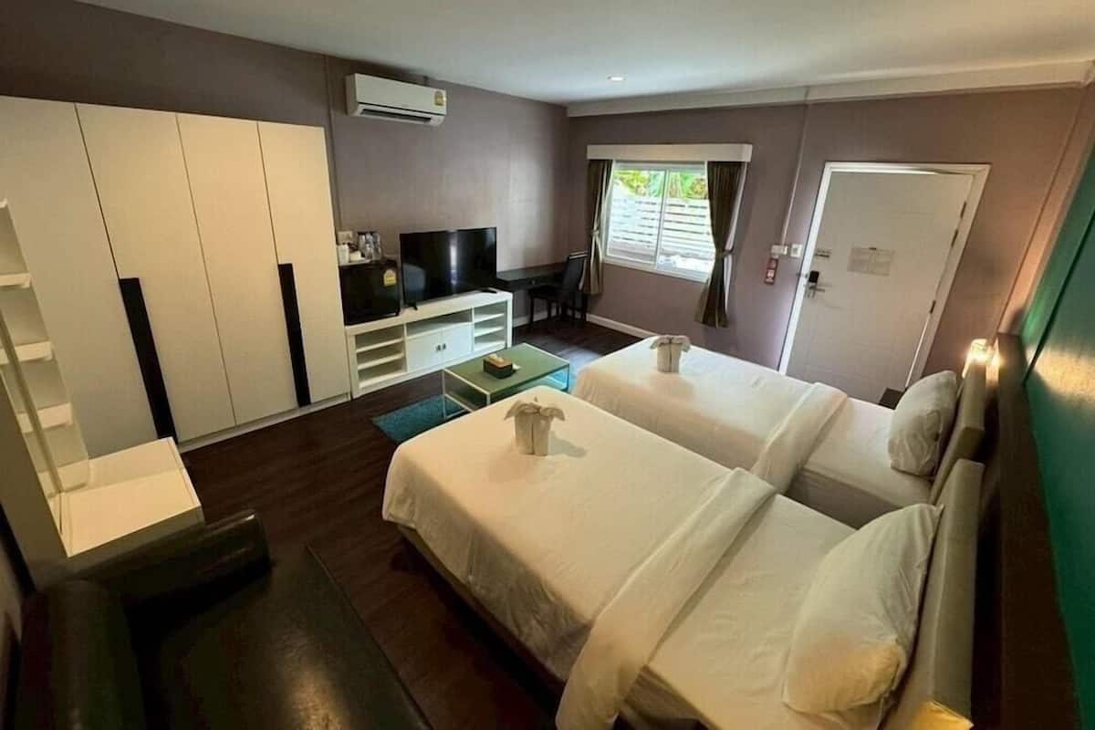 Une chambre d’hôtel avec deux lits, une télévision, une armoire et une fenêtre avec des rideaux.