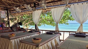 Ein Strandbereich für Massagen mit mehreren Massageliegen, jeweils mit Kissen und Korb.