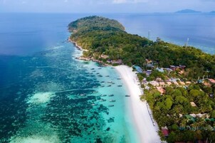 An aerial view of a coastal area with a beach, boats, and a forested island.