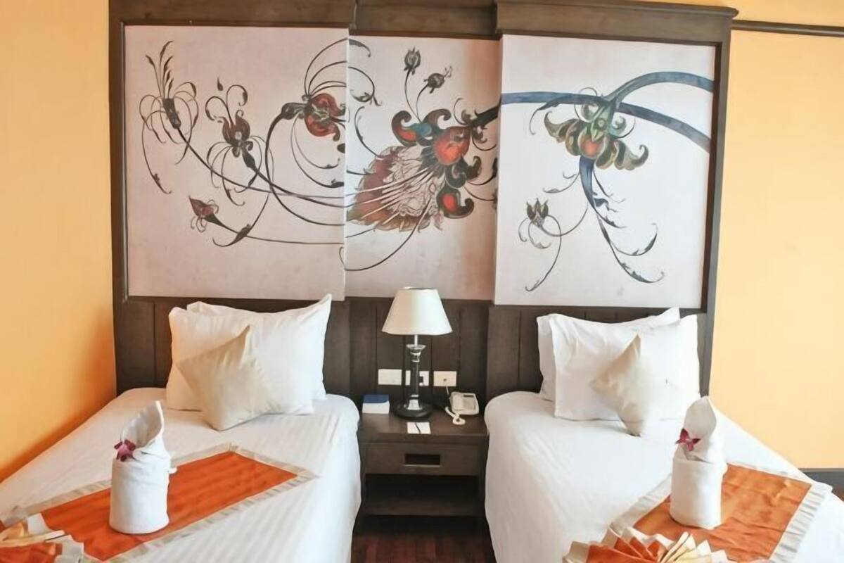 A hotel room with two beds, a nightstand with a lamp, and artwork on the headboard.