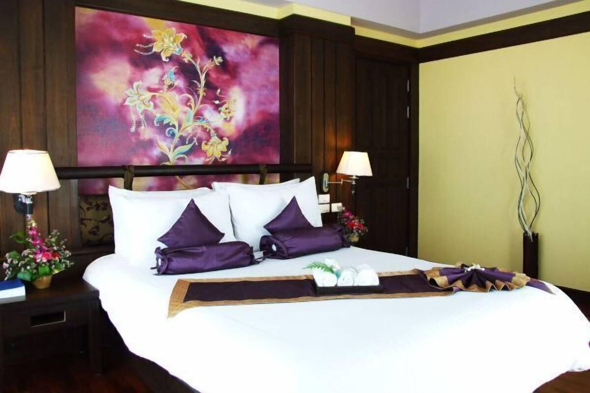 A hotel room with a large bed, two bedside lamps, a decorative painting, and a vase with flowers.
