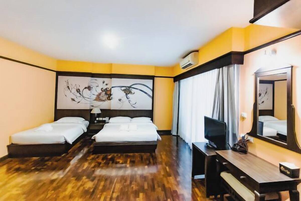 A hotel room with a wooden floor, two beds, a desk, a TV, and a large mirror.