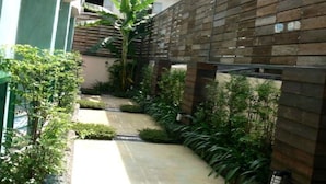 Un sendero estrecho bordeado por abundante vegetación y vallas de madera, que conduce a un edificio con fachada verde.